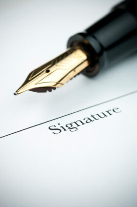 Pen resting above signature line of document. Focus on tip of pen nib.